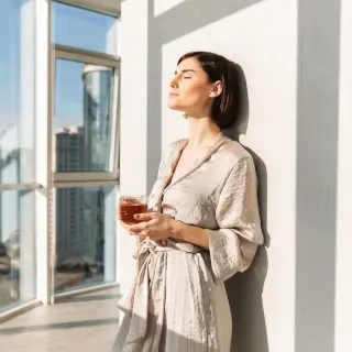 Frau steht mit einer Teetasse am Fenster