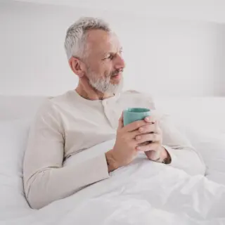 Mann sitzt mit Kaffeetasse im Bett