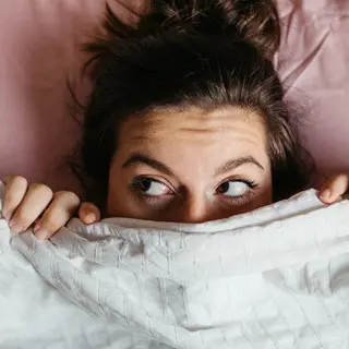 Frau blickt unter Bettdecke hervor