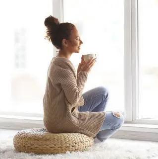 Frau sitzt mit einer Kafeetasse am Fenster
