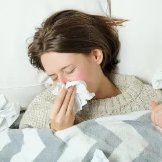 Frau im Bett schnäuzt sich die Nase