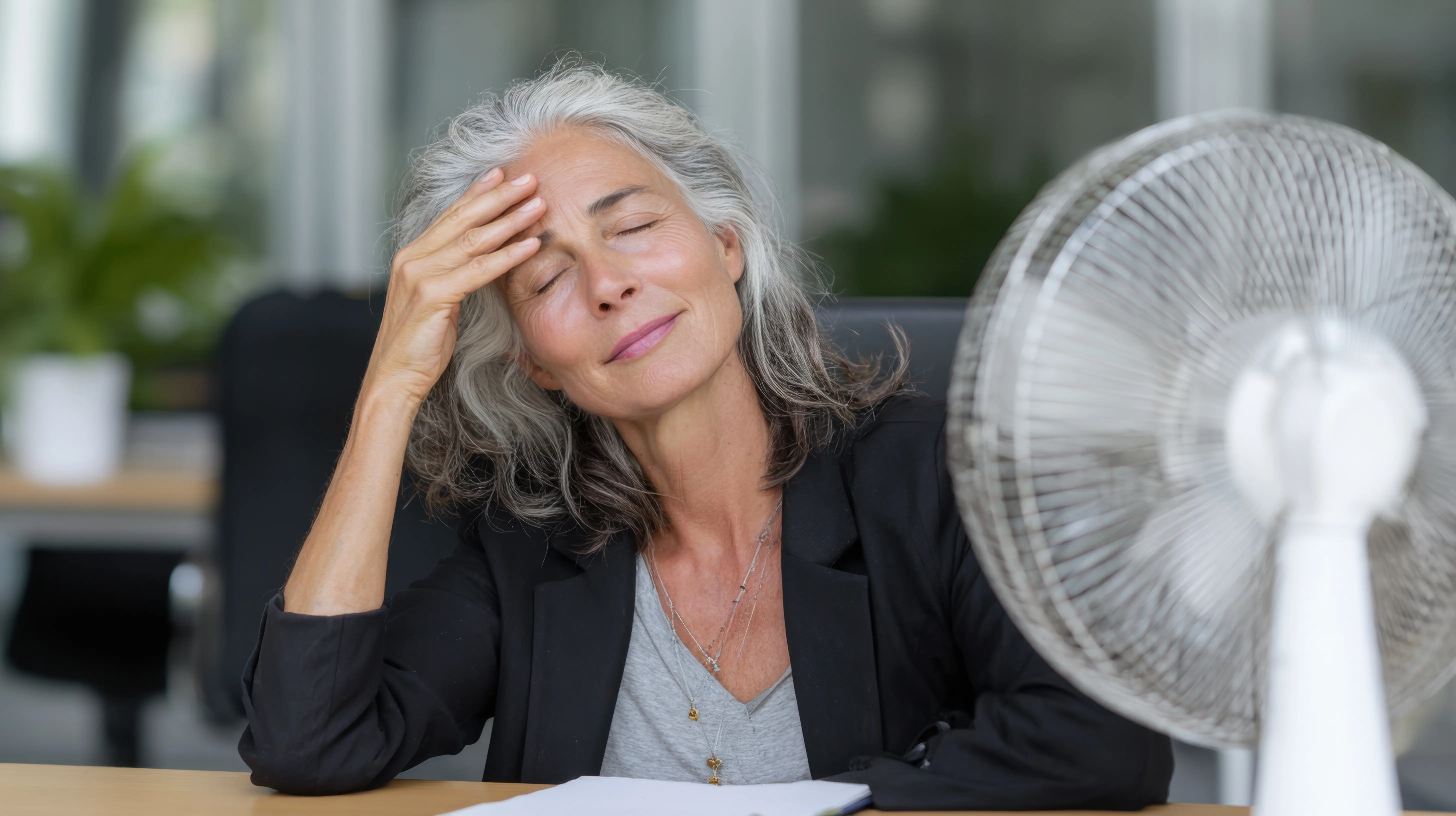 Frau mit Wechseljahresbeschwerden sitzt vor einem Ventilator
