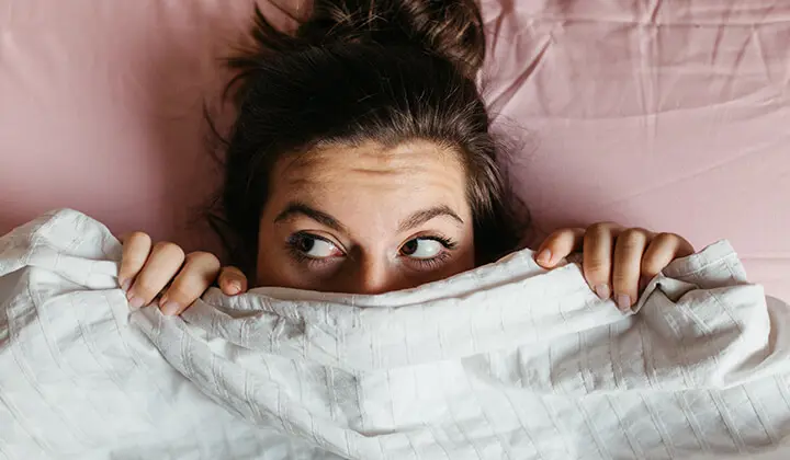 Frau mit Angst vorm Schlafen unter der Bettdecke 
