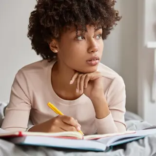 Frau liegt auf dem Bett und schreibt in ihr Schlaftagebuch