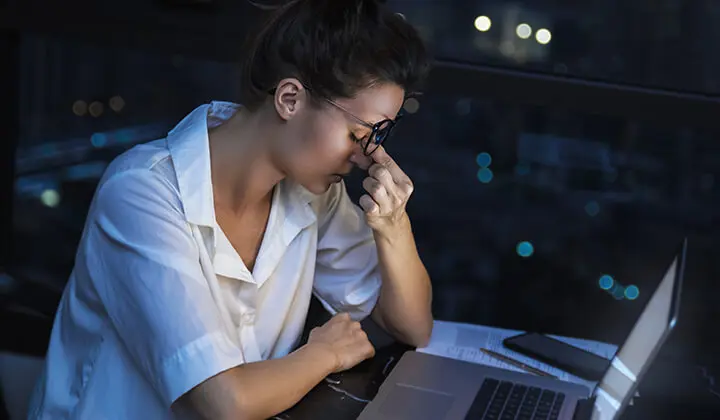 Frau sitzt abends müde am Laptop