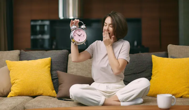 Frau hält Wecker und gähnt